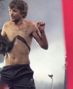 a man with no shirt on standing in front of a red and white wall holding a pair of gloves