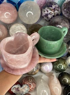 a hand is holding a small cup and saucer in front of many different colored rocks