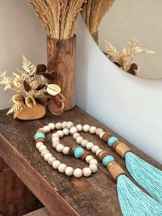 a wooden table topped with a tasseled necklace next to a vase filled with dried flowers