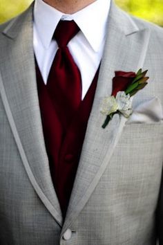 a man in a gray suit with a red tie and flower boutonniere