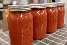 four jars filled with tomato sauce sitting on top of a table