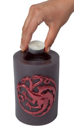 a hand holding a candle in front of a black container with red dragon designs on it