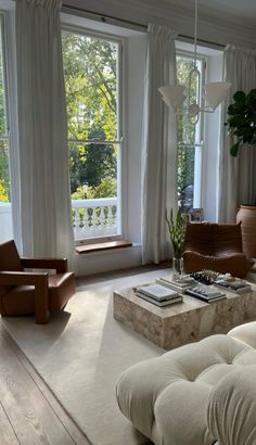 a living room filled with lots of furniture next to large windows covered in white curtains