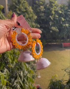 a person holding up two pairs of earrings in front of some trees and bushes with a building in the background