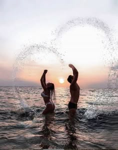 two people standing in the water with their arms up and one person throwing bubbles into the air