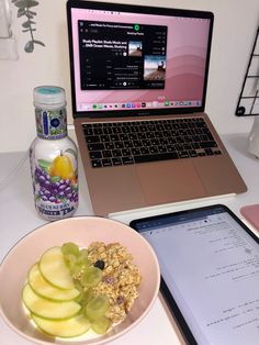 an open laptop computer sitting on top of a desk next to a bowl of fruit