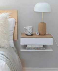 a nightstand with a lamp and some books on it next to a white bed in a bedroom