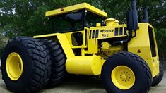 a large yellow construction vehicle parked on top of a dirt field with trees in the background