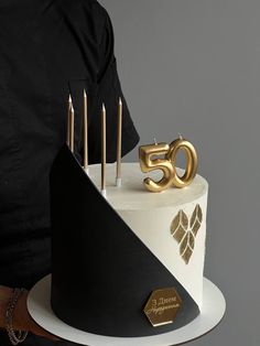 a white and black cake with gold numbers on the top is decorated with candles for fifty five