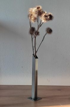 a metal vase with flowers in it on a wooden table next to a white wall