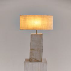 a lamp that is sitting on top of a block of concrete with a white shade