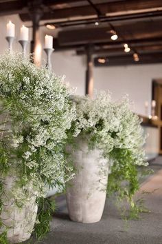 three white vases filled with flowers and greenery on top of a carpeted floor