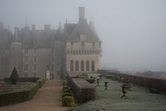 an old castle in the fog with lots of hedges and bushes on either side of it