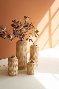 three wicker vases with flowers in them on a white table against an orange wall