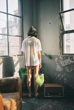 a woman standing in front of a window next to a couch and bird on the wall