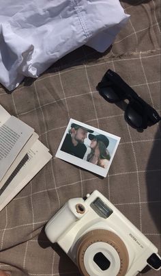 an open book, polaroid camera, sunglasses and other items on a bed sheet