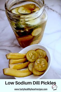 pickles in a bowl next to a jar of pickles on a marble table