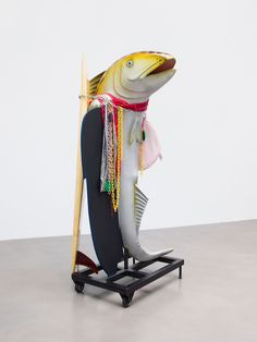 a sculpture of a fish holding a surfboard in its mouth and wearing a scarf