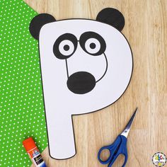 a paper cut out of a panda bear on top of a wooden table next to scissors and glue