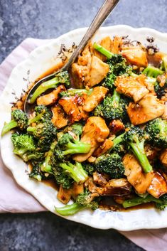 a white bowl filled with broccoli and chicken on top of a pink napkin