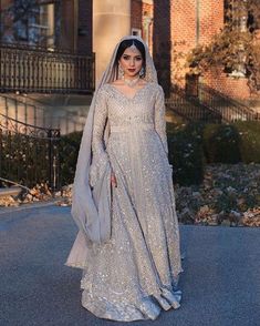 a woman in a silver gown and veil standing on the street with her hands behind her back