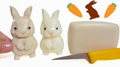 a hand holding a knife next to two small plastic rabbits and a block of butter