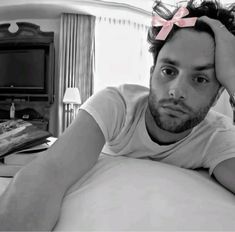 a man laying on top of a bed with a pink bow in his hair and looking at the camera