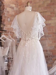 a wedding dress on display in front of a brick wall and mannequins