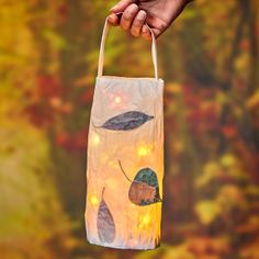 a hand holding a paper bag with leaves on it and string lights hanging from the handle