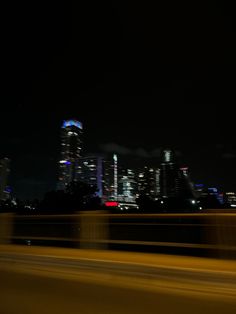 the city skyline is lit up at night with bright lights in the foreground and blurry cars on the road