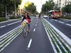 a woman riding a bike down the middle of a street next to tall buildings and trees