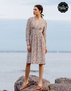 a woman standing on top of a rock next to the ocean with her hands in her pockets