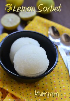 lemon sorbet in a black bowl on a yellow tablecloth with spoons