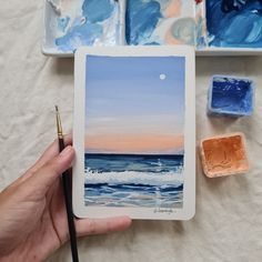 a person holding a paintbrush next to some watercolors