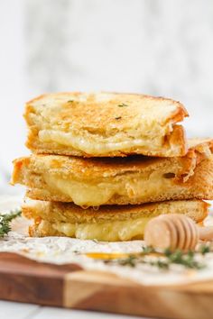 three grilled cheese sandwiches stacked on top of each other with honey in the background