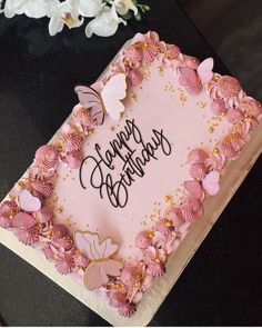 a birthday cake with pink frosting and butterflies on it, sitting on a table