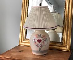 a lamp sitting on top of a wooden table next to a mirror with a heart painted on it