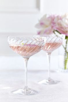 two wine glasses sitting on top of a table next to vases filled with flowers