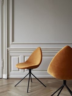 two orange chairs sitting next to each other on top of a hard wood floor in front of a white wall