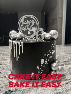 a black cake with white icing and silver balls on top that says happy birthday