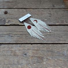 a pair of white and red fringe earrings on wooden planks with a tag attached to it