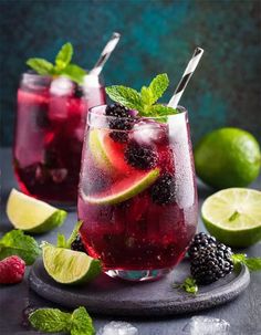 two glasses filled with blackberry limeade and blackberries on top of a slate platter