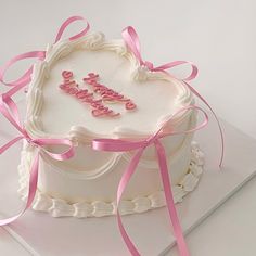 a heart shaped birthday cake with pink ribbon and name written on the frosted cake