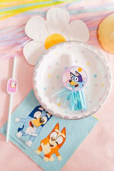 paper plates with cartoon characters on them are sitting on a pink surface next to other items