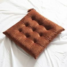 a brown square cushion sitting on top of a white sheet