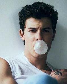 a man blowing bubbles on his nose while wearing a white t - shirt and looking at the camera