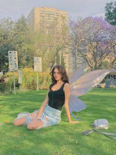 a woman sitting in the grass with a fairy wings on her chest and legs, posing for a photo