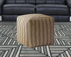 a striped ottoman sitting on top of a rug in front of a black leather couch