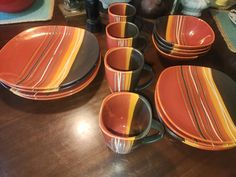 a wooden table topped with orange and black striped dinnerware on top of a wooden table