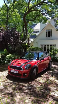 a small red car parked in front of a white house with trees and bushes around it